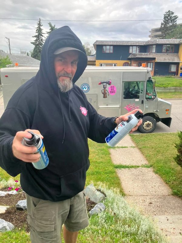 Rich of Lipstick Property Solutions in a Lipstick hoodie, holding two spray cans in front of the Lipstick truck in Prince George