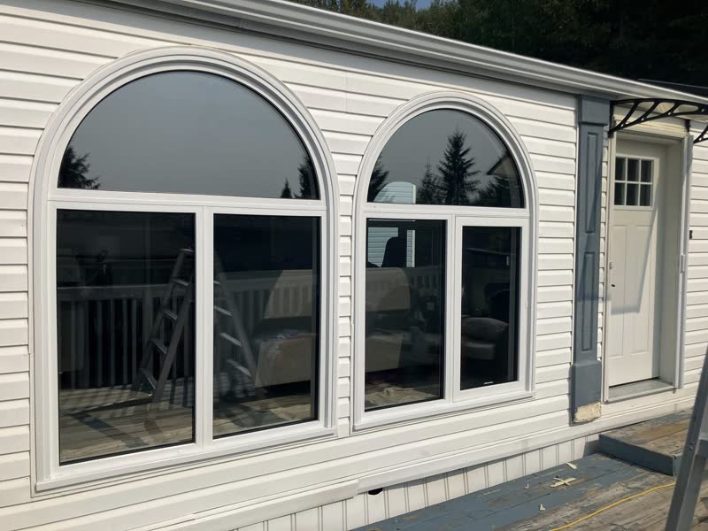 Twin arched picture windows installed on a white-sided home