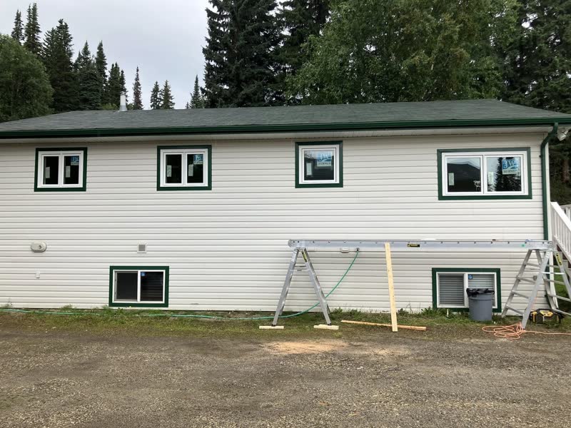 Green-trim windows going into a white bungalow, scaffolding still up