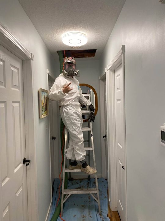 Insulation tech in a protective suit climbing into the attic hatch
