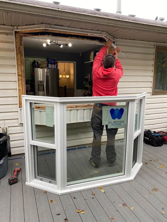 Crew lifting the new bay window into the opening from the deck