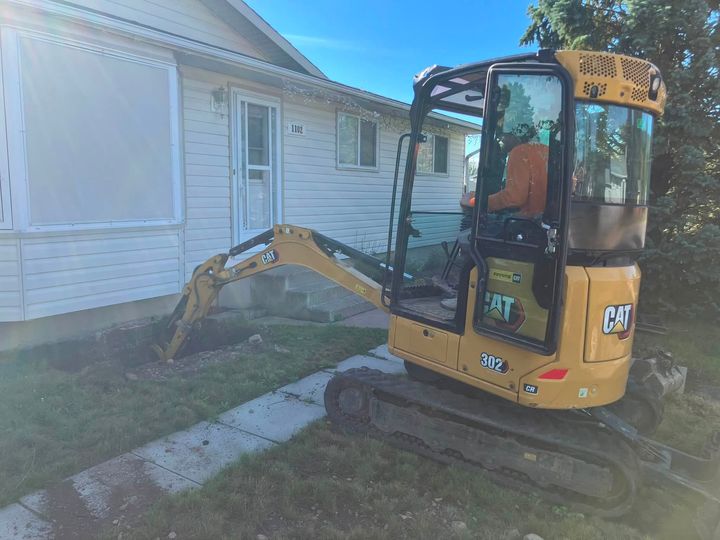 Mini excavator digging beside a white bungalow