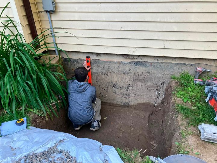 Installer digging beside the foundation of a beige-sided house